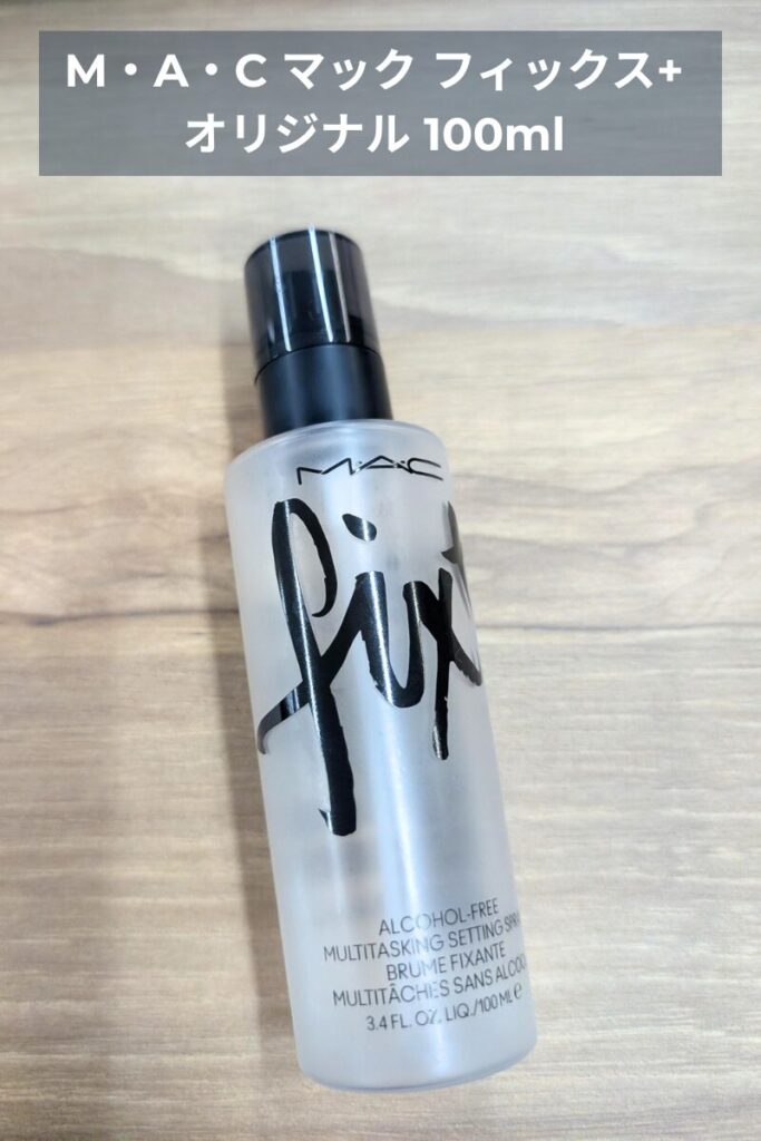 MAC フィックスプラス オリジナル 100ml のフェイスミストを、木目調のテーブル上で撮影した実物写真。香りと保湿でリフレッシュできる持ち運びに便利なセルフケアアイテム。